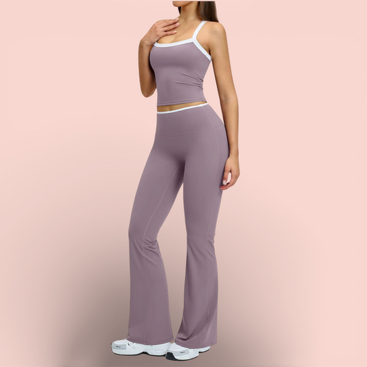 Woman wearing a mauve athleisure set with a fitted sleeveless crop top featuring white trim and high-waisted flared leggings, paired with white sneakers, standing against a soft neutral background.