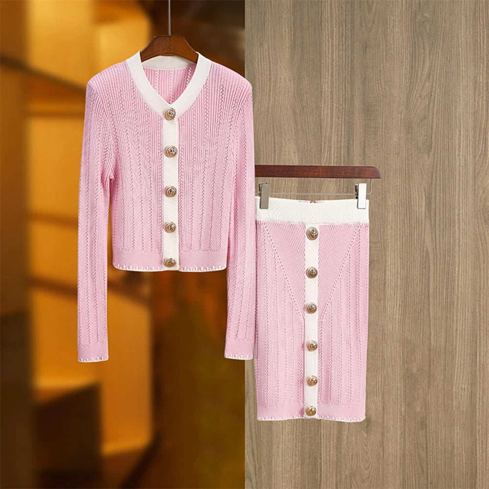 A two-piece knitting set in baby pink, consisting of a long-sleeved cardigan and a skirt, displayed on a wooden hanger and a flat surface.
